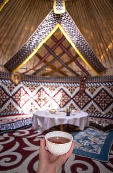 a cup of tea in a man's hand behind a dastarkhan in the Kazakh national yurt.