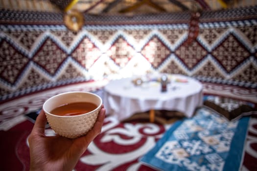 a cup of tea in a man's hand behind a dastarkhan in the Kazakh national yurt.