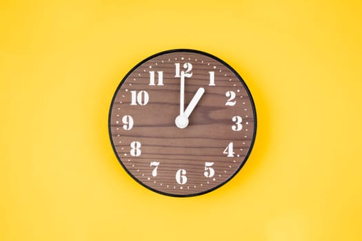 Retro wooden clock at 1 O' clock on yellow color background.