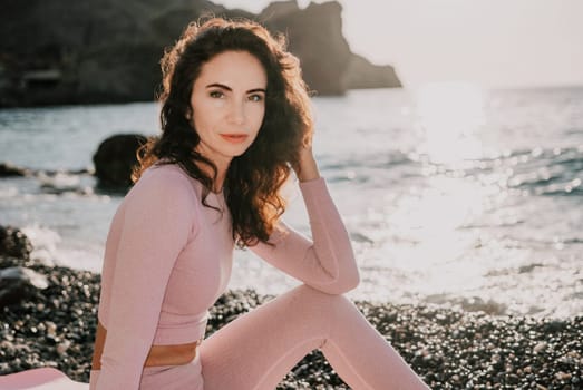 Young woman with black hair, fitness instructor in pink sports leggings and tops, doing pilates on yoga mat with magic pilates ring by the sea on the beach. Female fitness daily yoga concept