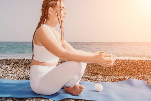 Woman yoga sea. Young woman with braids dreadlocks in white swimsuit and boho style braclets practicing outdoors on yoga mat by the ocean on sunny day. Women's yoga fitness routine. Healthy lifestyle, harmony