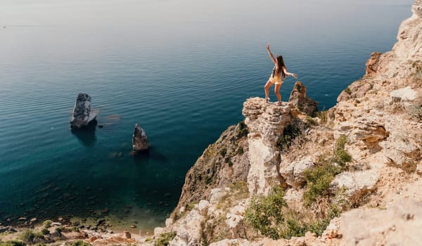 Woman travel sea. Happy tourist taking picture outdoors for memories. Woman traveler looks at the edge of the cliff on the sea bay of mountains, sharing travel adventure journey.