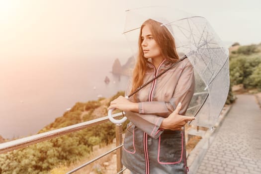 Woman rain park. Happy woman portrait wearing a raincoat with transparent umbrella outdoors on rainy day in park near sea. Girl on the nature on rainy overcast day