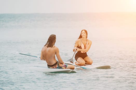 Sea woman and man on sup. Silhouette of happy young woman and man, surfing on SUP board, confident paddling through water surface. Idyllic sunset. Active lifestyle at sea or river