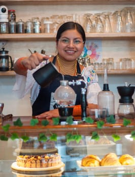 native barista woman pouring water into japanese coffee pot looking at camera. High quality photo