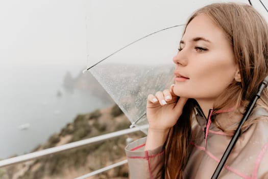 Woman rain park. Happy woman portrait wearing a raincoat with transparent umbrella outdoors on rainy day in park near sea. Girl on the nature on rainy overcast day