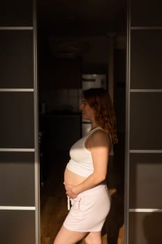 A pregnant woman in shorts and a crop top stands in profile between folding doors