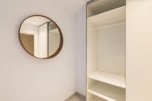 Close-up of a corner of a room with a mirror and an open empty wardrobe in light beige tones. The concept of a comfortable compact apartment after renovation.