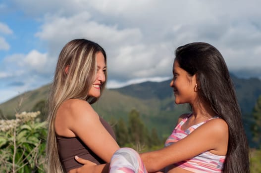 mother and daughter looking at each other in the middle of nature with sportswear together in the sunset of a summer day on vacation. High quality photo