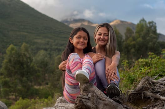 mother and daughter sitting on the trunk of a tree looking at the camera in the middle of nature. High quality photo