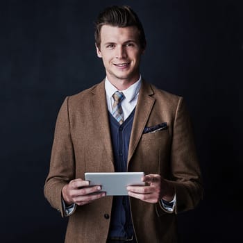 Technology only added to my success. Studio shot of a young businessman using his tablet against a dark background