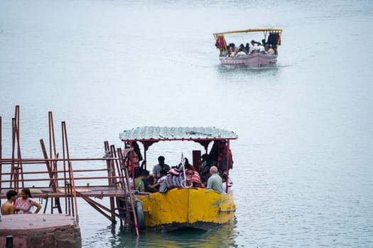 Rishikesh, haridwar, India - circa 2023: People boarding an old and broken ferry boat that runs across the river ganga shows the worn out and unsafe boats that tourists travel by