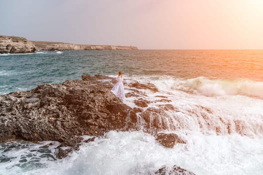 A woman stands on a rock in the sea during a storm. Dressed in a white long dress, the waves break on the rocks and white spray rises