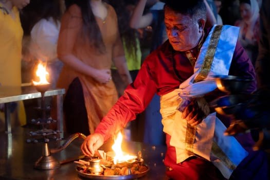 Rishikesh, India - 29th Apr'23: hindu priest sitting on the bank of ganga river lit from one side by the fire from an oil lamp a key component in Hinduism religion in India