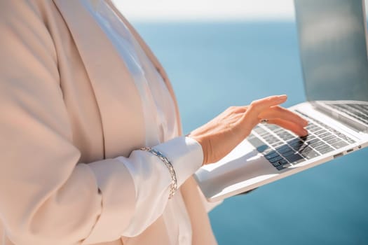 Freelance women sea working on the computer. Good looking middle aged woman typing on a laptop keyboard outdoors with a beautiful sea view. The concept of remote work