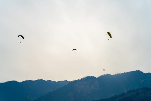 multipel parasailing gliders against sunset sky and mountains with copy space and bright colors showing freedom in hill station in India