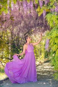 Woman wisteria lilac dress. Thoughtful happy mature woman in purple dress surrounded by chinese wisteria.