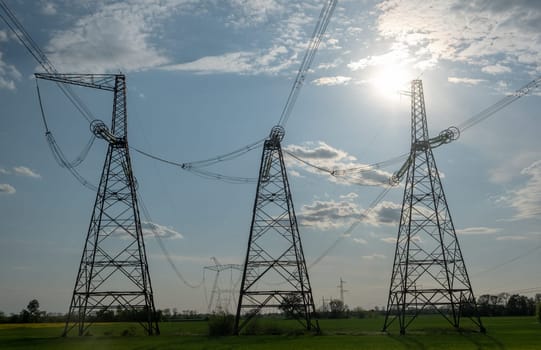 Electric pole and high voltage lines in the field with white cloudy and blue sky.