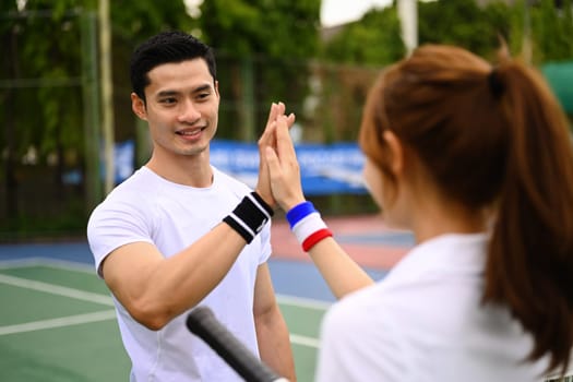 Fitness sport tennis couple giving each other a high five while playing tennis together on a court.