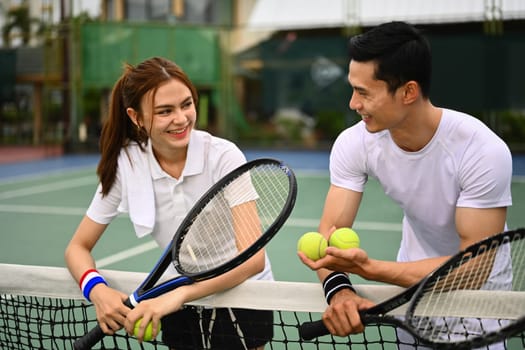 Male and female tennis players talking and resting after game over net at court. Sport activity, tennis training and competition.