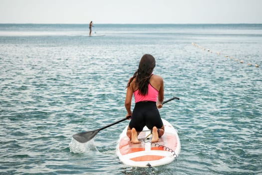 Sea woman sup. Silhouette of happy young woman in pink bikini, surfing on SUP board, confident paddling through water surface. Idyllic sunset. Active lifestyle at sea or river. Slow motion