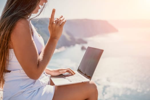 Successful business woman in yellow hat working on laptop by the sea. Pretty lady typing on computer at summer day outdoors. Freelance, travel and holidays concept.