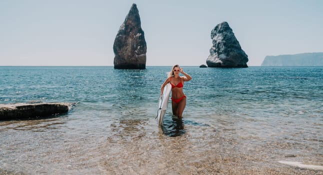 Close up shot of beautiful young caucasian woman with black hair and freckles looking at camera and smiling. Cute woman portrait in a pink bikini posing on a volcanic rock high above the sea