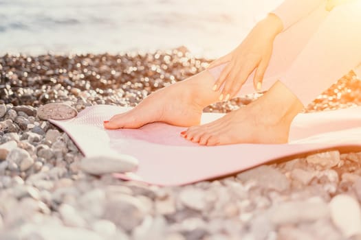 Young woman with black hair, fitness instructor in pink sports leggings and tops, doing pilates on yoga mat with magic pilates ring by the sea on the beach. Female fitness daily yoga concept