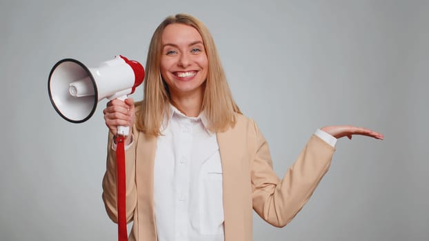 Business woman talking with megaphone, proclaiming news, loudly announcing advertisement, warning using loudspeaker to shout speech, pointing empty place. Copy-space. Girl on gray wall background