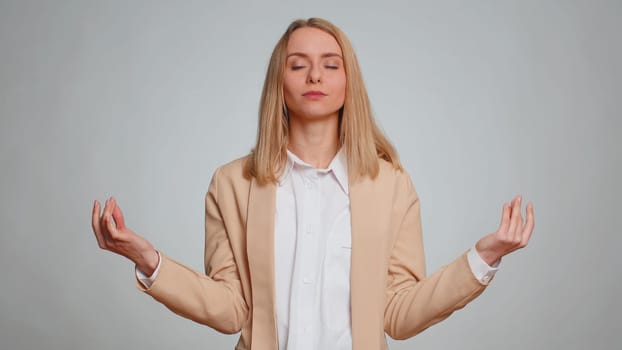 Keep calm down, relax, inner balance. Business woman breathes deeply with mudra gesture, eyes closed, meditating with concentrated thoughts, peaceful mind. Female girl in suit on gray background