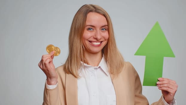Businesswoman show golden bitcoins indicating up arrow sign successful exchange rate increase. Achievement career wealth cryptocurrency investment mining BTC future technology. Girl on gray background