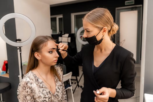 Make-up artist paints eyebrow pencil to beautiful brunette in be