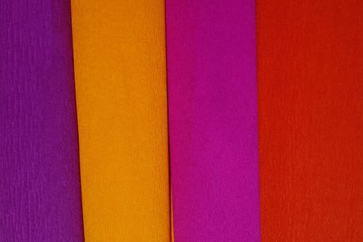 Rolls of crepe paper lying next to each other in the colors purple, red, orange, lilac