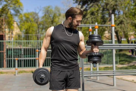 Athletic lebanese man in sportswear doing arms weight lifting dumbbells exercises, pumping up arm bicep muscles. Young guy on playground. Sports, health, fitness routine, workout. Strength motivation