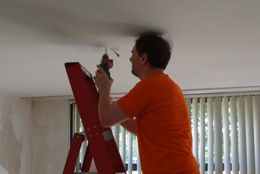 A man drills a hole in the ceiling for the lamp he wants to hang