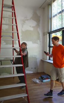 Two modern men plan a job. The eldest looks at the ceiling, the younger uses his smartphone.
