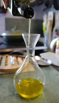 Pouring olive oil into an oil dispenser. Kitchen utensils in the background