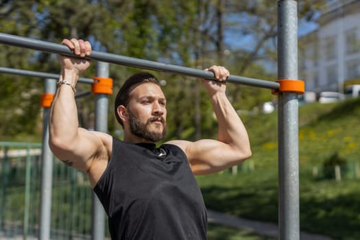 Athletic lebanese man in sportswear doing pull ups exercises on horizontal bar. Young guy pumping up back muscles on summer playground. Sports, health, fitness routine, workout. Strength, motivation