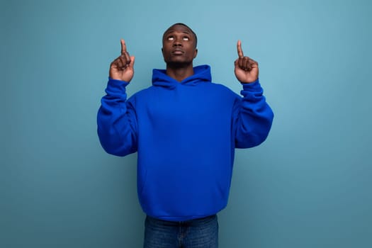 energetic positive young african man consultant in stylish hoodie shows with hand actual offer on studio background with copy space.