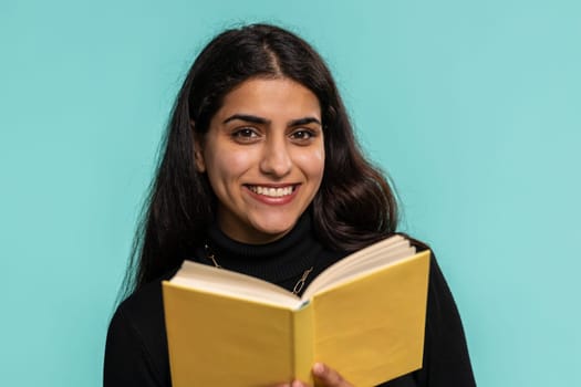 Happy indian woman reading funny interesting fairytale story book, leisure hobby, knowledge wisdom, education, learning, study, wow. Pretty hindu girl isolated alone on blue studio wall background