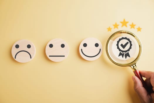 Hand holds magnifier, focusing on happy smiley face icon among various emotions. Good feedback rating and positive customer review, satisfaction survey, mental health. Certificate of satisfaction.