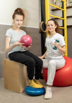 Smiling Child, Child With Disability Does Physical Exercises With Support Of Rehabilitation Specialist, Physical Therapist In Gym. Rehabilitation. Vertical plane. High quality photo