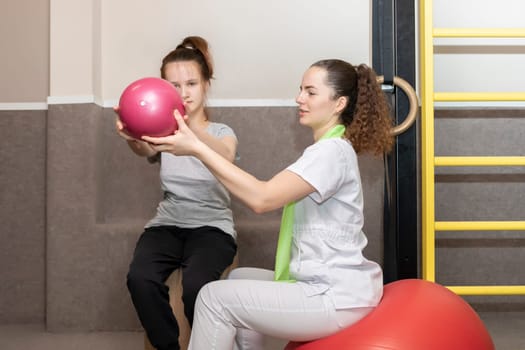 Smiling Girl, Child With Disability Does Physical Exercises With Ball With Support Of Rehabilitation Specialist, Physical Therapist In Gym. Rehabilitation. Horizontal plane. High quality photo