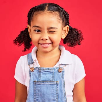 Portrait, wink and a black child on a red background in studio having fun or feeling carefree. Kids, fashion and smile with a happy female child winking inside on a color wall while looking funny.