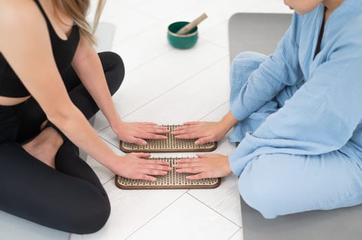 Two women sit on yoga mats with their hands on sadhu boards