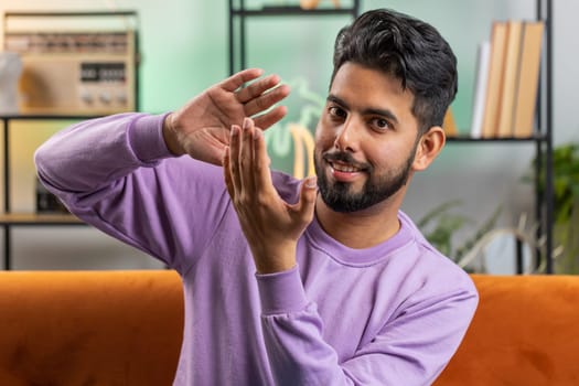 Cheerful happy rich indian man showing wasting, throwing money around hand gesture, more tips earnings, big profit, win lottery, body language, share, celebrate. Guy at home in living room apartment