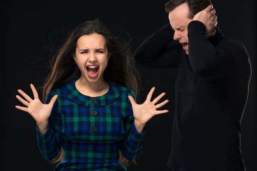 ouple having conflict, bad relationships. Angry fury woman screaming man closing his ears on black background