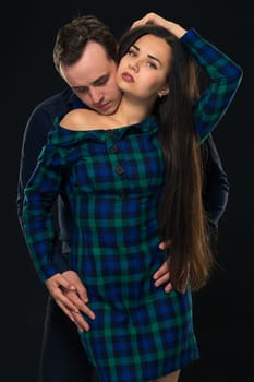Couple posing in studio. On black background. Young woman in blue checkered dress