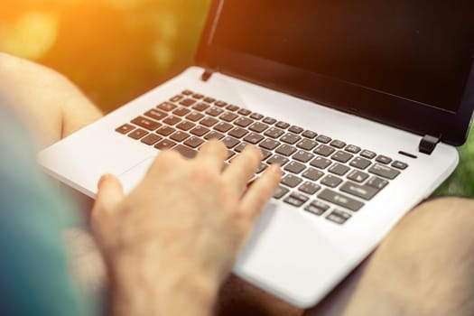 Top view male hands using notebook outdoors in urban setting while typing on keyboard, businessman freelancer working on computer while sitting on city park bench, tourist working on laptop, filter. Sun flare