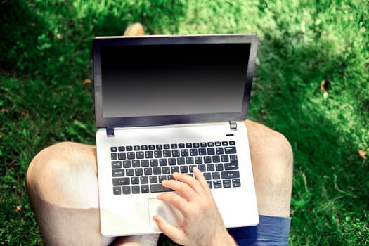 Young blogger sitting on grass and working with laptop. Copy space